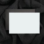 Blank black and white card on textured black cloth, ideal for designs.