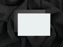 Blank black and white card on textured black cloth, ideal for designs.